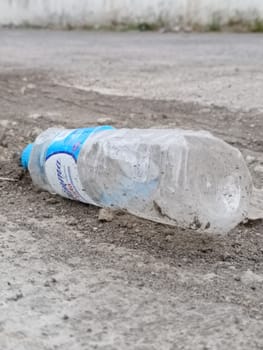 A crumpled plastic bottle lies on gravel, highlighting environmental pollution. This image represents littering, waste, and the need for ecological awareness and recycling efforts.