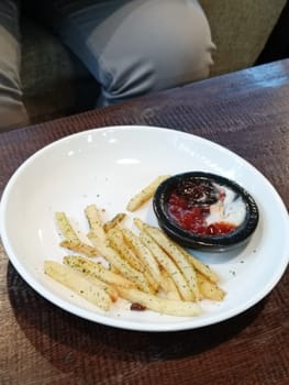 A bowl of savory French fries seasoned with herbs, accompanied by ketchup and mayonnaise, served on a rustic wooden table. Perfect for snack time or a casual dining setting.