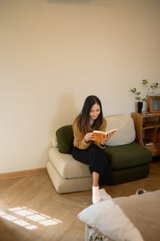 Serene young woman spending a peaceful day with book on sofa at home.