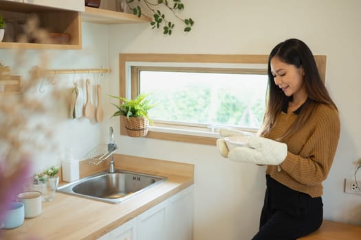 Smiling woman holding a freshly Baked dish with oven mitts.