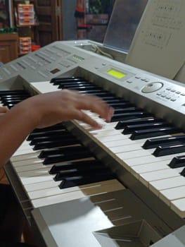 Close-up of young hands skillfully playing an electronic organ, capturing a moment of musical practice and creativity in a cozy music room.