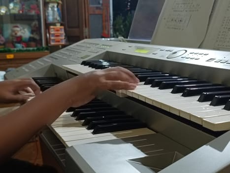 Close-up of young hands skillfully playing an electronic organ, capturing a moment of musical practice and creativity in a cozy music room.
