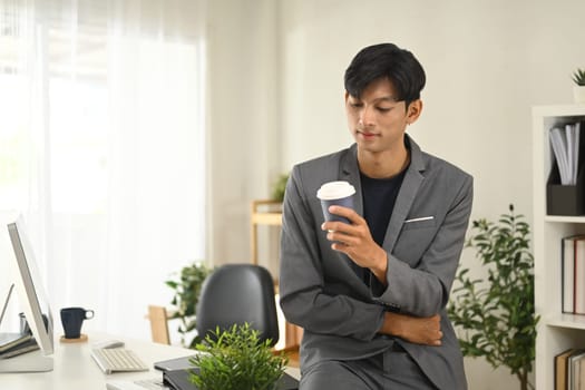 Young businessman in suit taking a coffee break at his office.