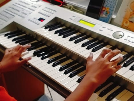 Close-up of young hands skillfully playing an electronic organ, capturing a moment of musical practice and creativity in a cozy music room.