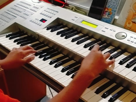 Close-up of young hands skillfully playing an electronic organ, capturing a moment of musical practice and creativity in a cozy music room.