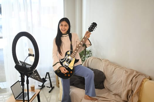 Young cheerful woman playing electric guitar during a live session.