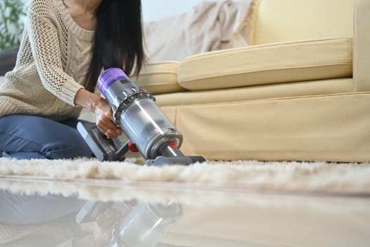 Close up of woman cleaning carpet with a cordless vacuum in her home.
