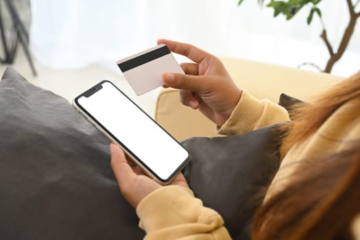 Close up of a woman using her smartphone and credit card for online purchases.