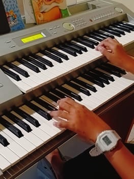 Close-up of young hands skillfully playing an electronic organ, capturing a moment of musical practice and creativity in a cozy music room.