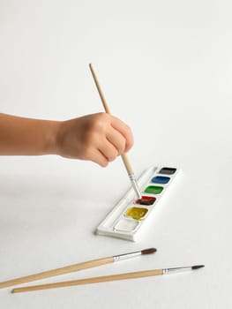 Hand holding brush painting with watercolor palette on white background.
