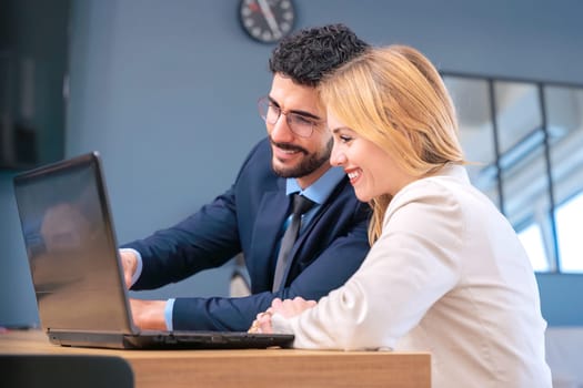 Two business colleagues collaborate in a modern office, smiling as they work together on a laptop. They share ideas in a professional yet friendly environment, fostering productivity and teamwork.