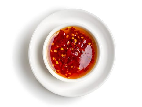 A white bowl of red chili sauce with chili flakes on a white plate, aerial view