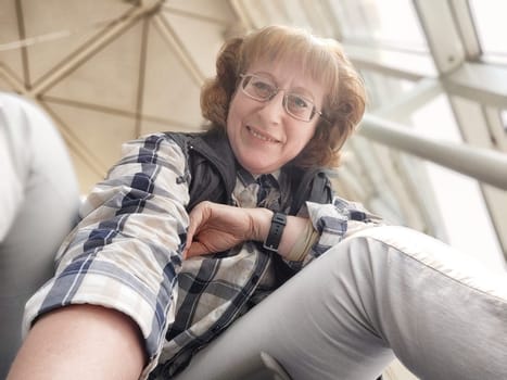 A cheerful middle-aged woman takes a selfie in the airport terminal, capturing the moment as she waits for her departure. The atmosphere is lively and bright.