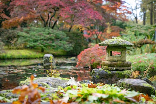 A tranquil Japanese garden showcasing a moss-covered stone lantern surrounded by vibrant autumn foliage and a reflective pond, embodying peace and natural beauty in a serene setting