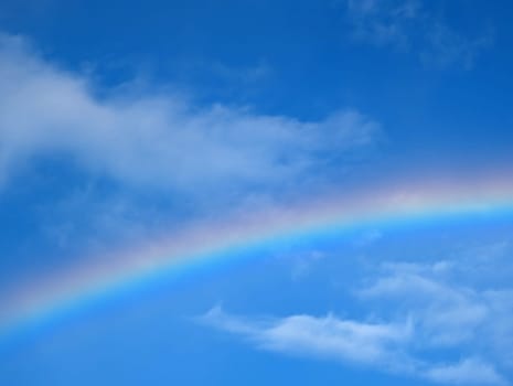 Following a short rain shower, a colorful rainbow stretches across the sky, contrasting beautifully with the bright blue backdrop and soft clouds.