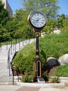 Boston - May 30, 2010: A beautifully crafted clock tower sits beside stone steps, surrounded by lush greenery in the park, creating a picturesque atmosphere on a sunny day.