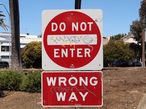 San Francisco - August 19, 2010: A no entry sign, covered in graffiti with the words wrong way, stands in an urban setting amidst trees, reflecting a vibrant day with clear skies.