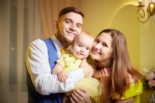 Family portrait with a young girl in yellow dress in a decorated room with floral arrangements