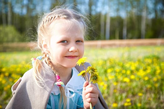 A cheerful girl gathers dandelions in a vibrant yellow flower field on a sunny spring day, radiating happiness and innocence.