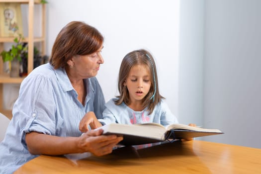 Grandmother and granddaughter sit closely, reading book together, sharing quiet and heartwarming moment in comfort of their home