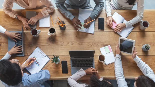 Office lifestyle concept. Top view of international young business team having meeting at office, sitting around table
