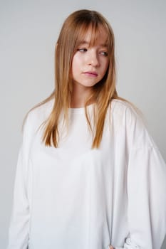 Casual portrait of a young girl wearing a white long-sleeve shirt and blue jeans in a minimalist studio close up