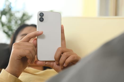 Young woman relaxing in living room and checking notifications on smartphone.