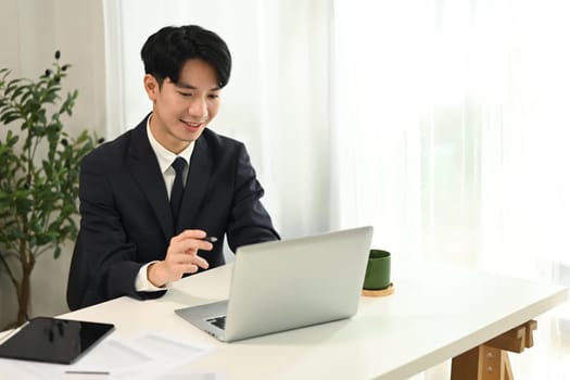 Smiling businessman in black suit working with laptop at office.
