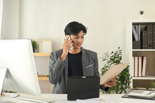 Young businessman having pleasant phone conversation at his office desk.