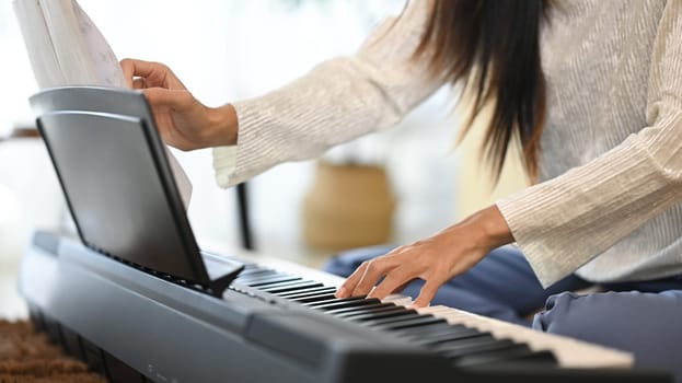 Cropped shot young woman playing electric piano on carpet in living room.