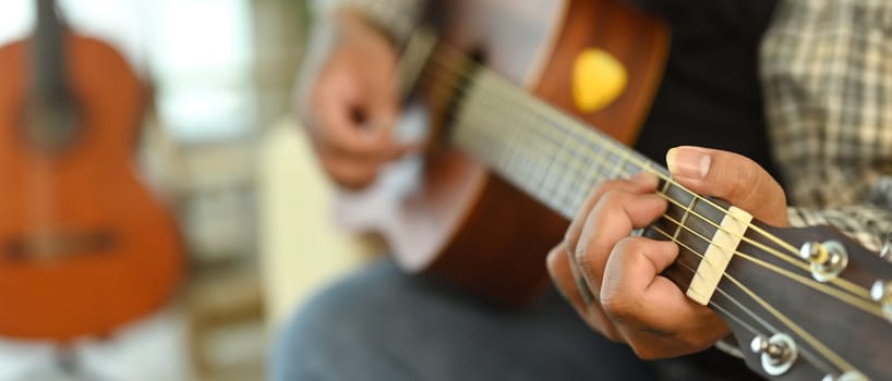 Close up of young man playing acoustic guitar. Leisure activity and hobby concept.