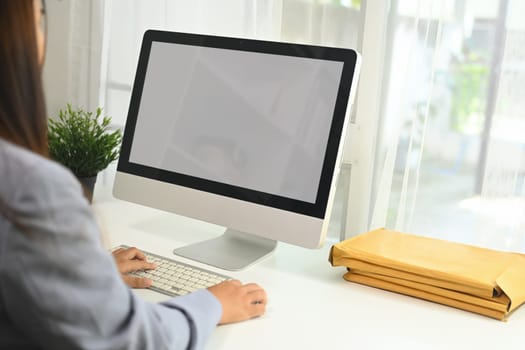 Side view of young businesswoman sitting at a desk with a computer monitor in front of her.