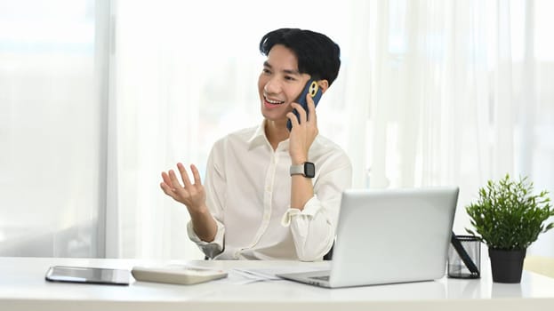 Young businessman having pleasant phone conversation at his office desk.