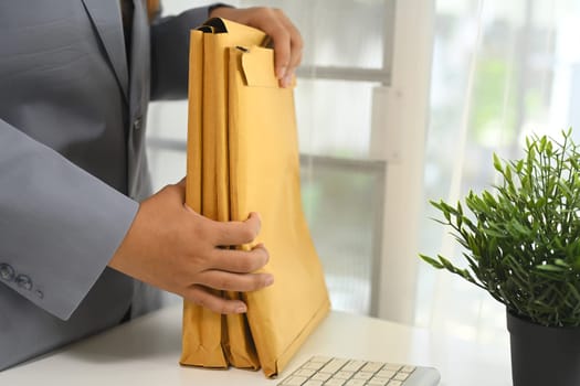 Cropped shot of businessperson organizing important documents in envelopes at office desk.