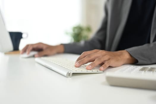 Close up of businessman typing on wireless keyboard at modern workspace.