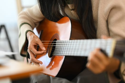 Young beautiful woman playing acoustic guitar in the living room.
