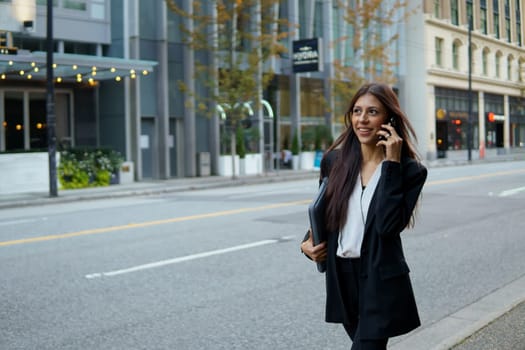 Young hispanic businesswoman talking on her cell phone while walking on city urban street.