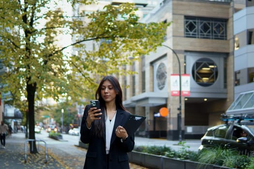Confident businesswoman checking her smartphone while walking in the city.