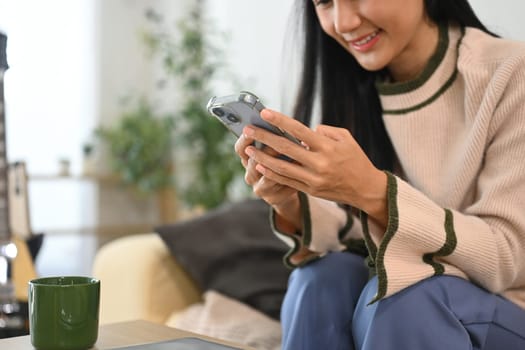 Young woman relaxing in living room and checking notifications on smartphone.
