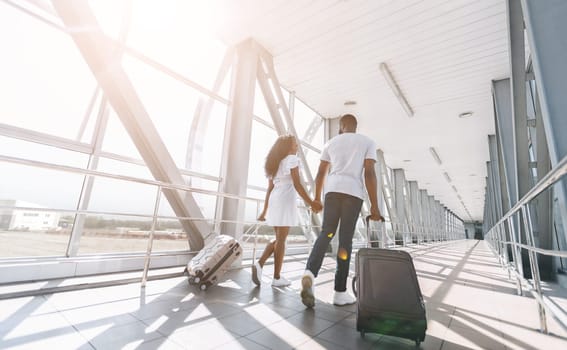 Going to flight. Young african couple walking with luggage at airport building, empty space