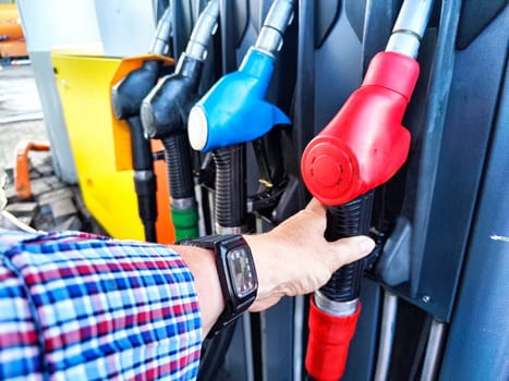 A person is using a red fuel nozzle to refuel their car at a service station during daylight hours.