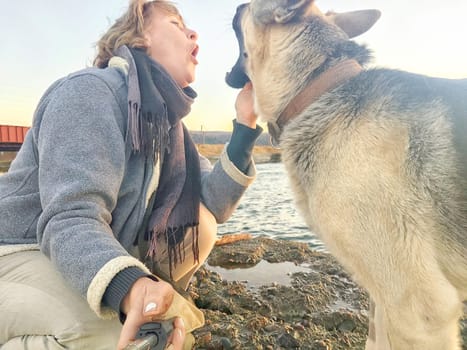 Adult girl with shepherd dog taking selfie near water of lake or river. Middle aged woman and big pet on nature. Friendship, love, fun, hugs