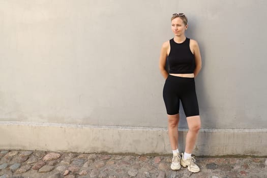 Full-length portrait of a posing female athlete posing against a gray wall.