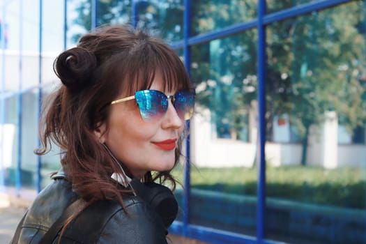 Beautiful girl in blue sunglasses in profile against a glass wall.