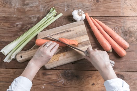 An overview of cutting carrots on a cutting board with celery and garlic on the table.