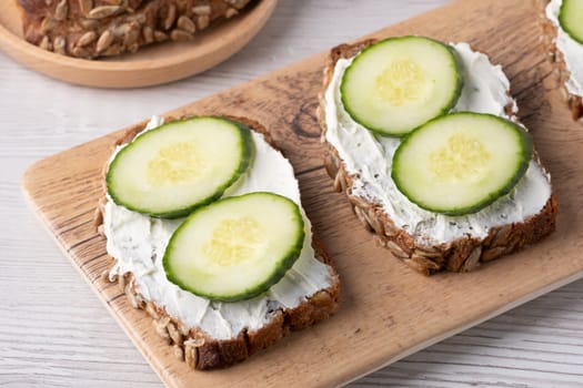 Slices of whole grain bread topped with cream cheese and fresh cucumber arranged beautifully at a rustic wooden table.