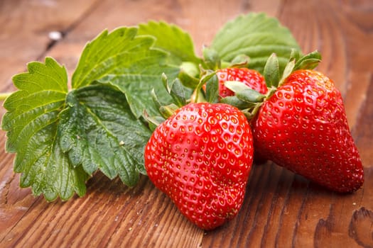 Ripe strawberries and strawberry leaves in a studio on wood.