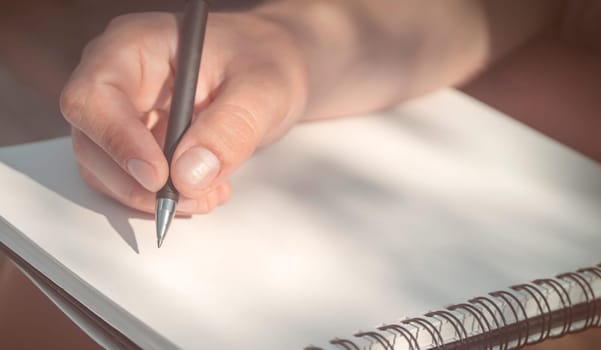 A man takes notes, sketches or makes a plan on a blank white sheet of paper in an album, a businessman, aspiring writer or student holds a notepad and a black pen, close-up view.