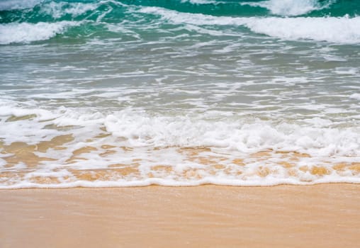 Beautiful clean beach with golden yellow sand and clear turquoise ocean water with waves. Picturesque coastline without people on a sunny day.
