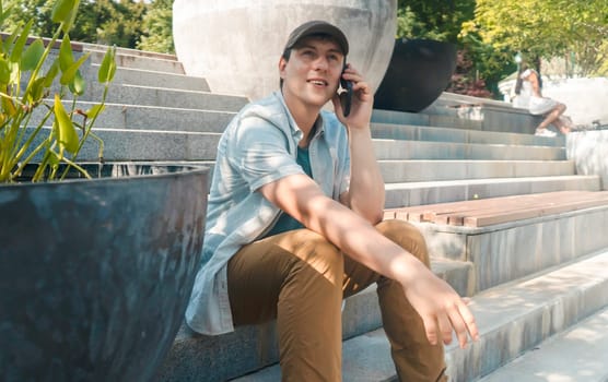 A young cheerful man with a smiley face talks on the phone in a park on a sunny day, a happy successful man communicates on a smartphone with friends, negotiates on a business, project or study.